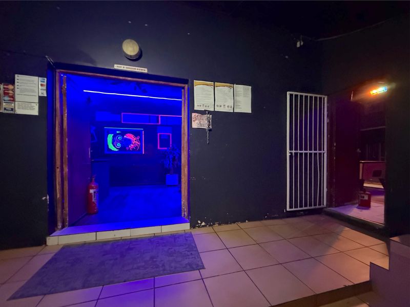Commercial entrance area featuring tiled flooring, security gate, and wall-mounted fire safety equipment, illuminated with blue accent lighting.