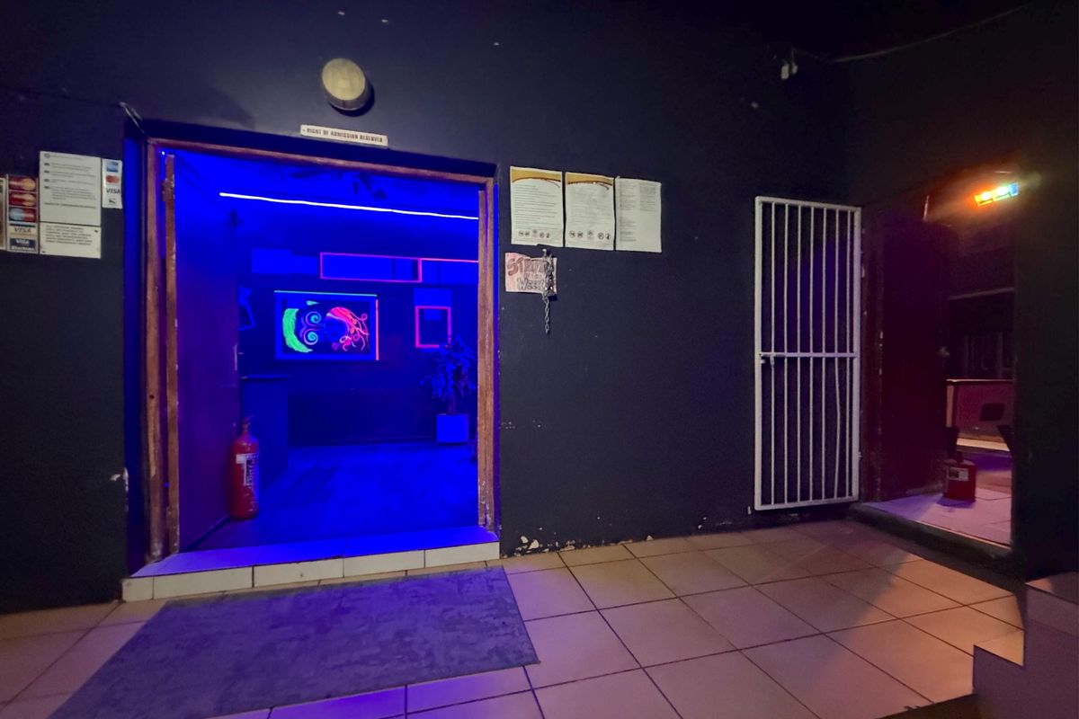 Commercial entrance area featuring tiled flooring, security gate, and wall-mounted fire safety equipment, illuminated with blue accent lighting.