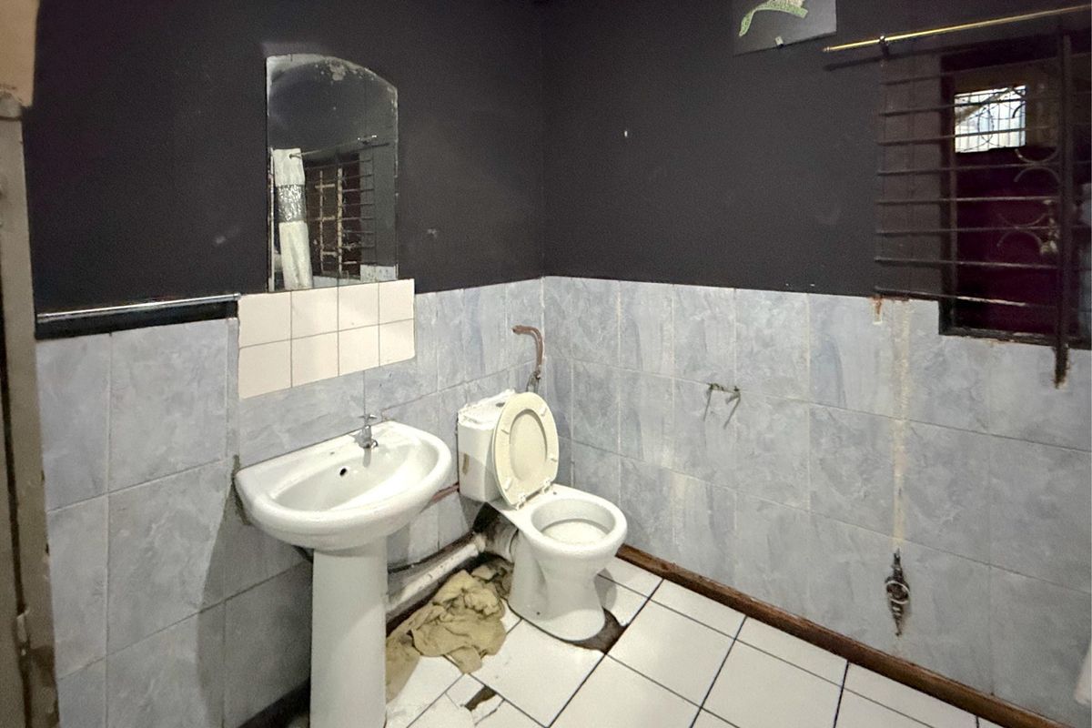 A dated bathroom featuring a pedestal basin and toilet, with significant wear to the floor and wall tiling requiring renovation.