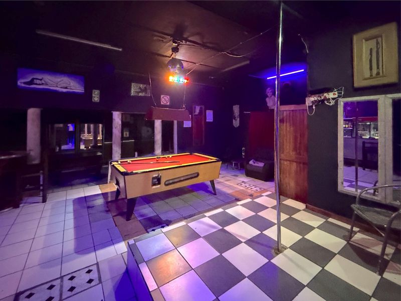 Commercial bar area featuring a built-in stage with a dance pole, checkered flooring, and ambient lighting fixtures.