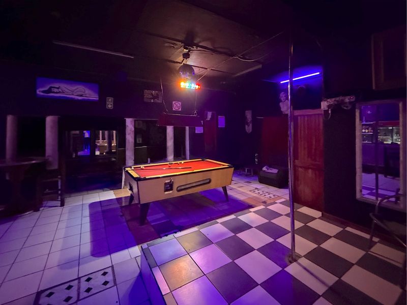 Commercial bar area featuring a checkered tile floor, built-in stage with dance pole, and integrated entertainment lighting.