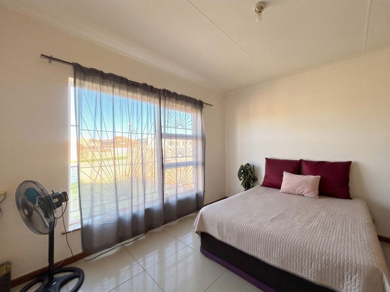 A bedroom featuring tiled flooring, a large window with security bars, and coved ceiling detailing.