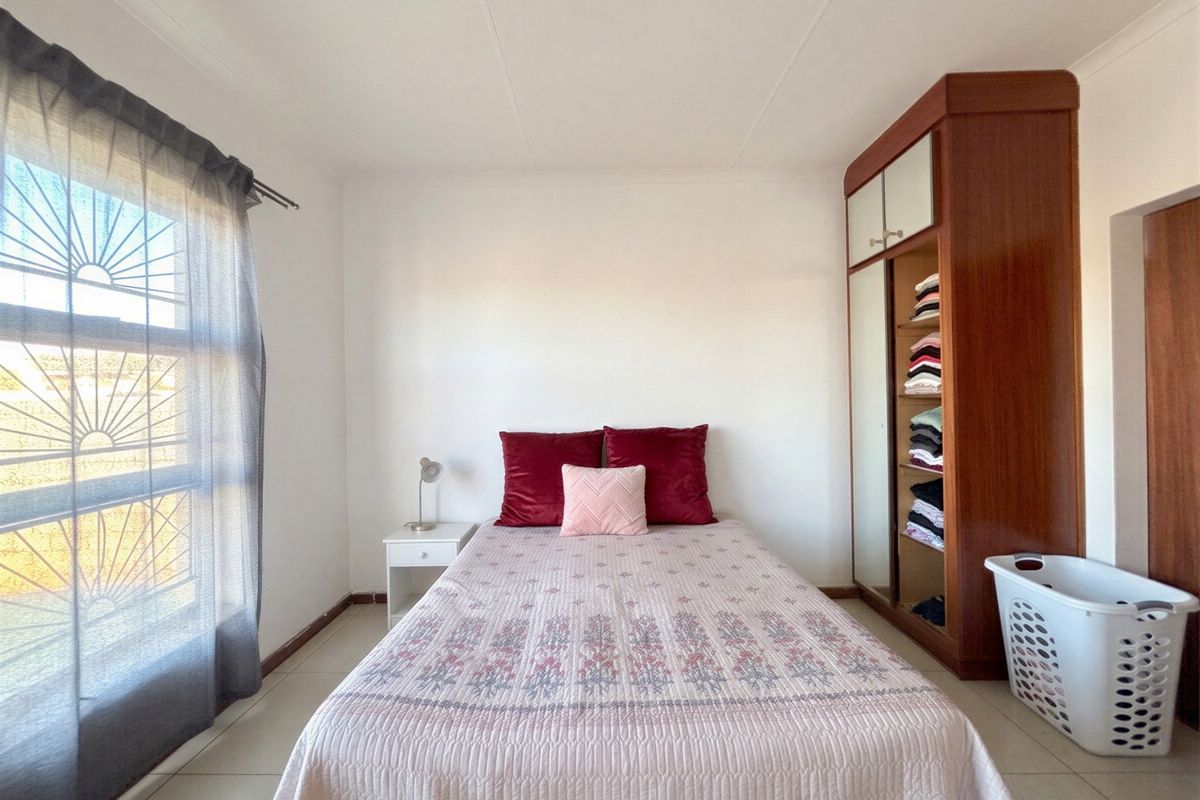 A functional bedroom featuring tiled flooring, a built-in wooden wardrobe, and a window fitted with security bars.