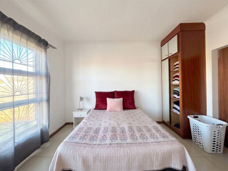 A functional bedroom featuring tiled flooring, a built-in wooden wardrobe, and a window fitted with security bars.