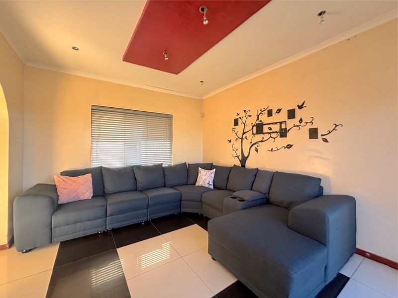 A living room featuring a decorative recessed ceiling panel, tiled flooring, and venetian blinds, currently requiring minor electrical finishing.