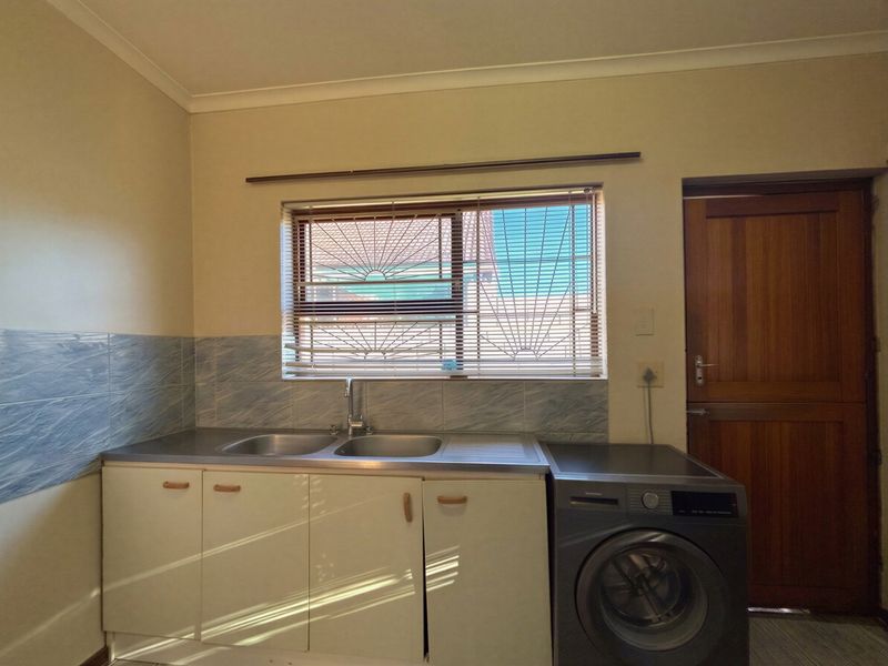 A functional laundry area featuring a stainless steel double sink, built-in cabinetry, tiled splashback, and direct access via a timber door.