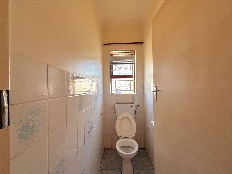 A compact, dated bathroom featuring a standard toilet, tiled walls, and tiled flooring, offering potential for a modern renovation.