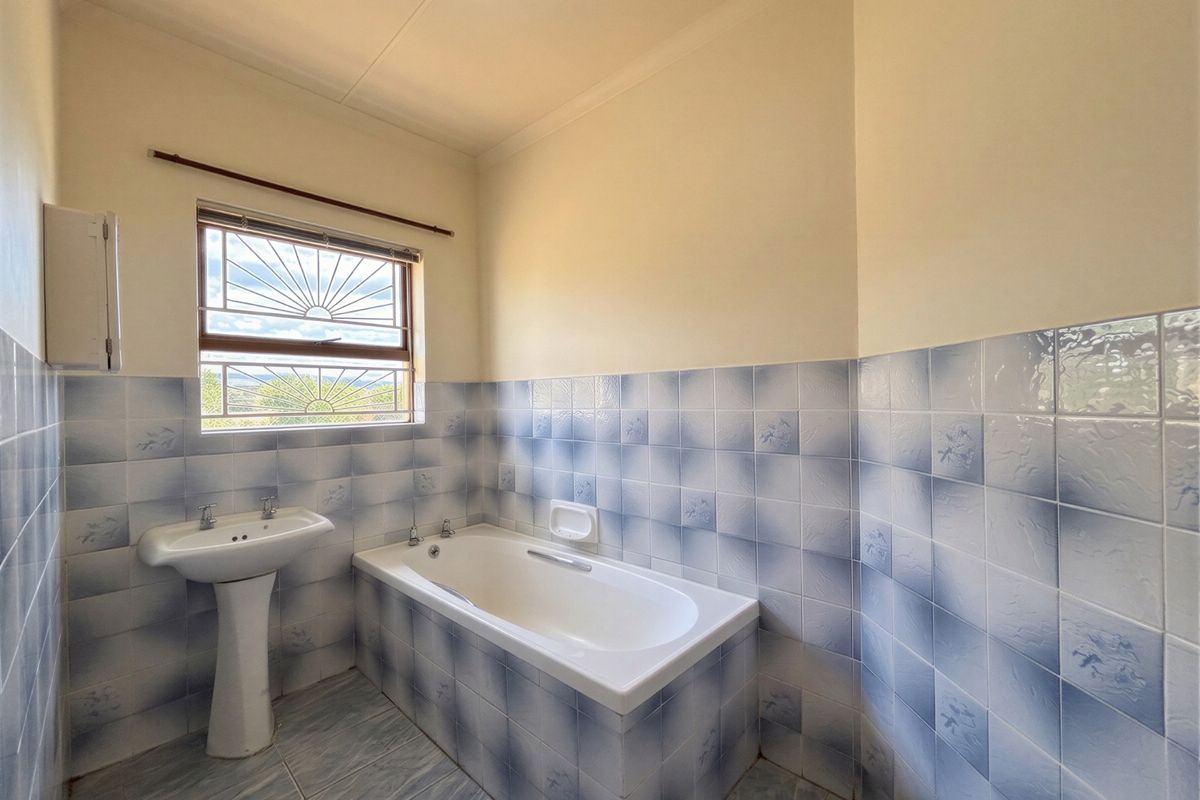A functional bathroom featuring a pedestal washbasin, a built-in bathtub, and blue-patterned wall tiles.