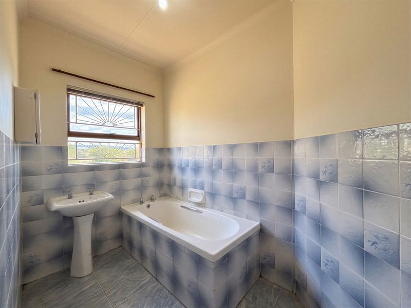 A functional bathroom featuring a pedestal washbasin, a built-in bathtub, and blue-patterned wall tiles.