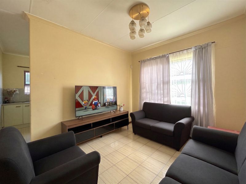 A functional living room featuring tiled flooring, security bars on the windows, and a central ceiling light fixture.