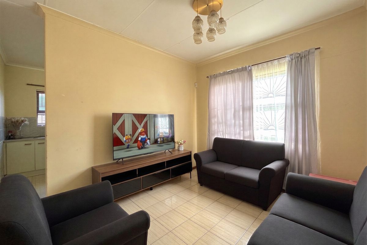 A functional living room featuring tiled flooring, security bars on the windows, and a central ceiling light fixture.
