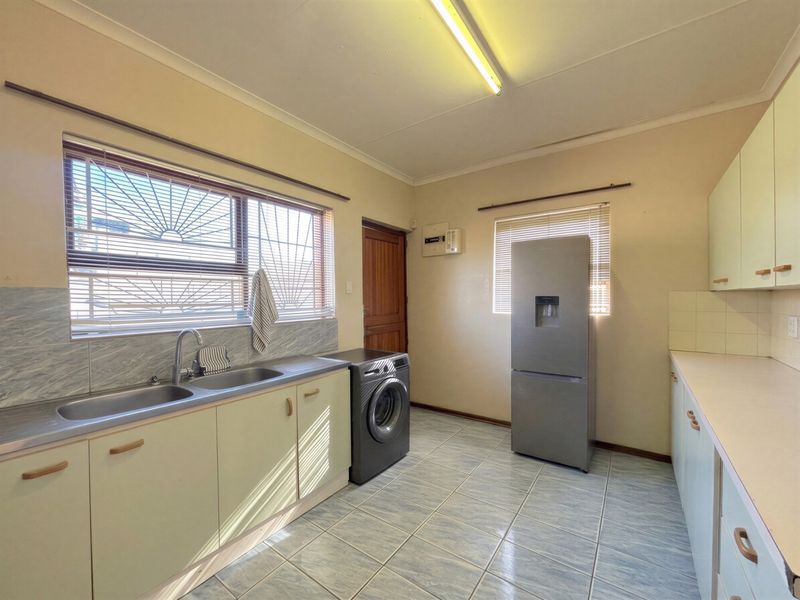 Functional laundry room featuring tiled flooring, built-in cabinetry, and a double stainless steel sink with security bars on the windows.
