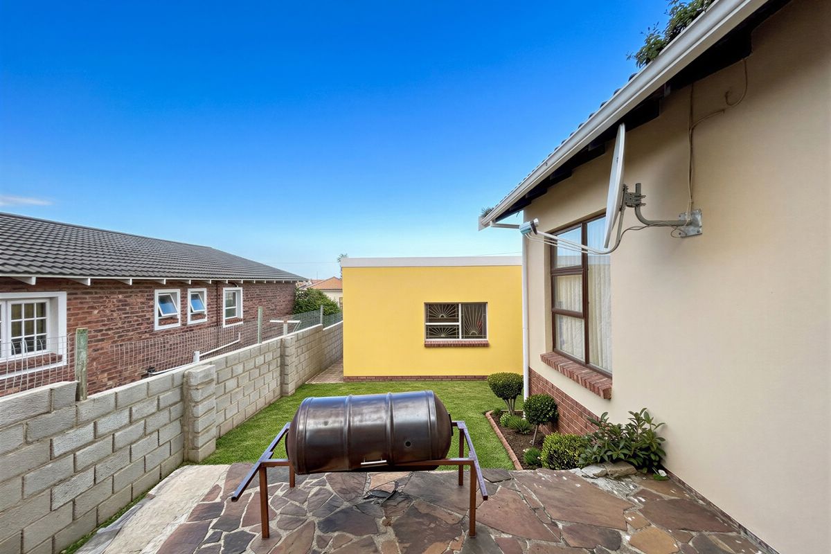 Rear exterior view featuring a stone-paved patio, small lawn area, and concrete block boundary wall.