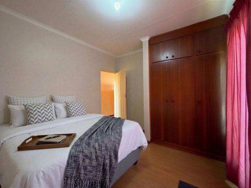 A bedroom featuring laminate flooring and a large built-in wooden wardrobe with overhead storage compartments.