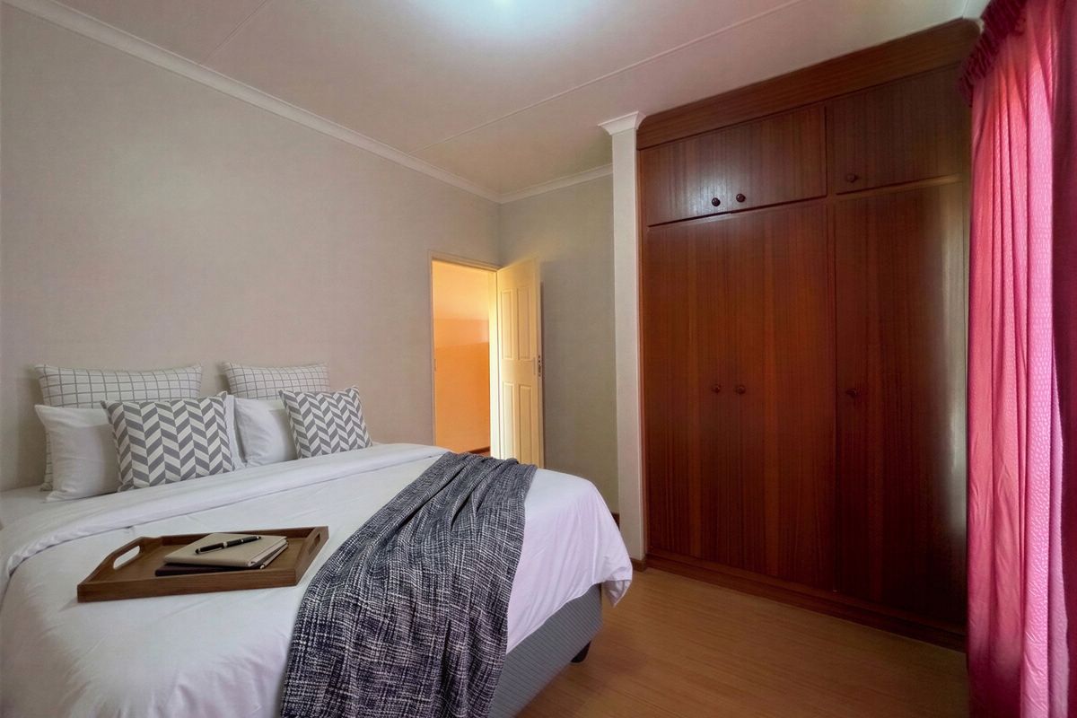 A bedroom featuring laminate flooring and a large built-in wooden wardrobe with overhead storage compartments.