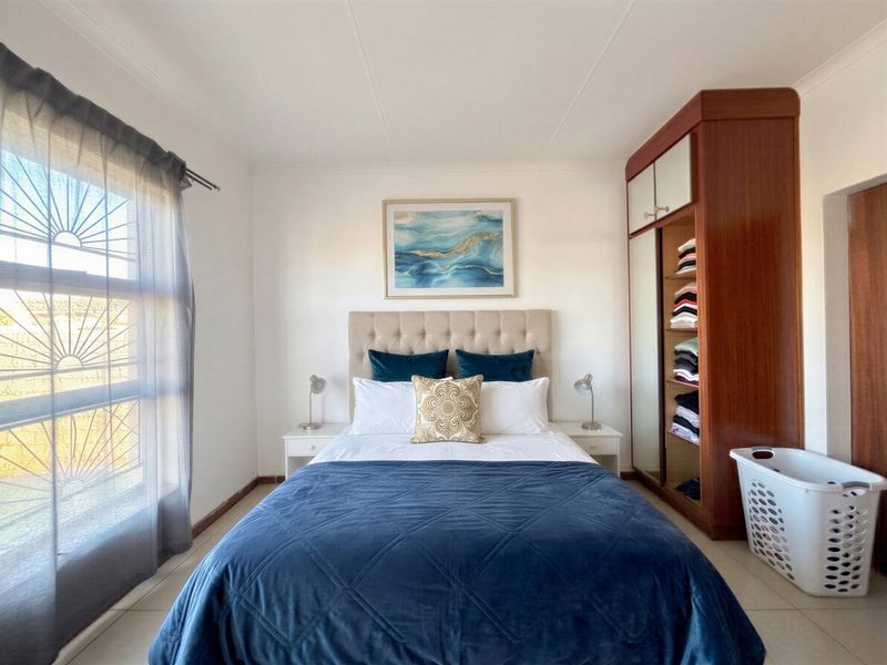 A well-maintained bedroom featuring tiled flooring, a built-in wardrobe, and a large window with security bars for added safety.