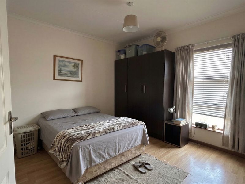 A functional bedroom featuring laminate flooring, a built-in wardrobe, and natural light through window blinds.