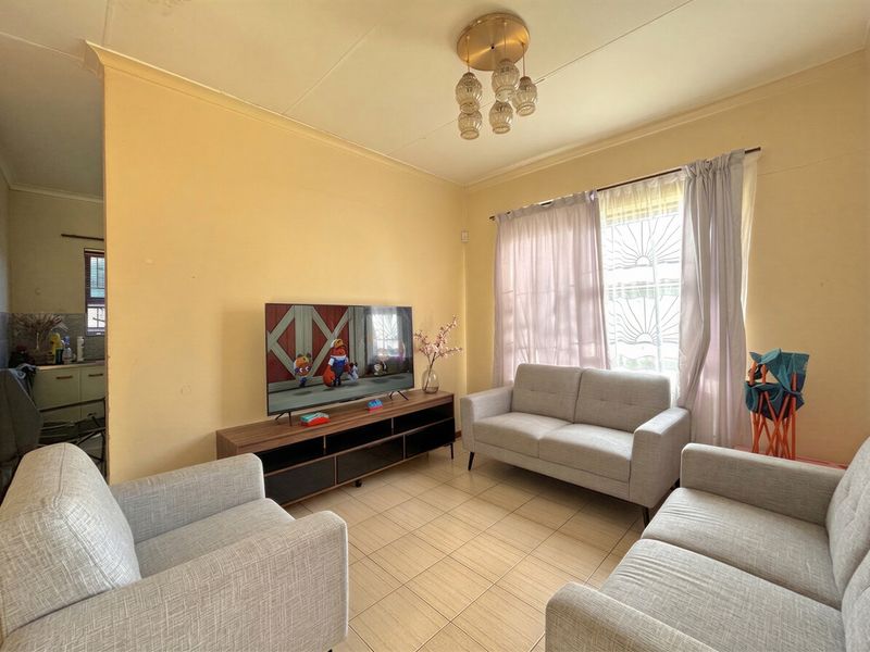 A functional living room featuring tiled flooring, a decorative ceiling light, and a window fitted with security bars.