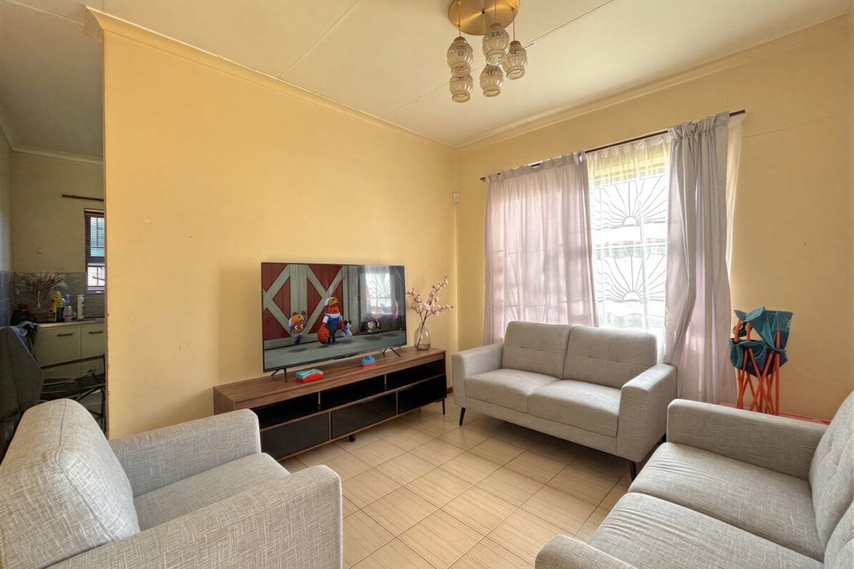 A functional living room featuring tiled flooring, a decorative ceiling light, and a window fitted with security bars.
