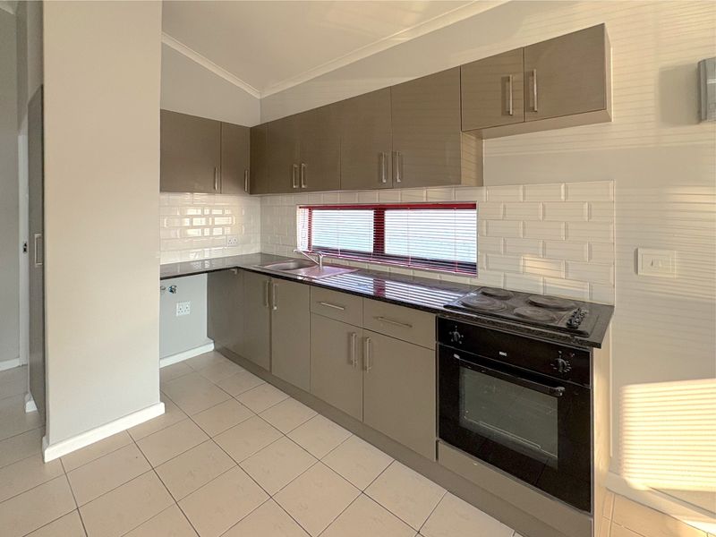A clean, modern kitchen featuring neutral-toned cabinetry, granite countertops, a subway tile backsplash, and integrated electric cooking appliances.