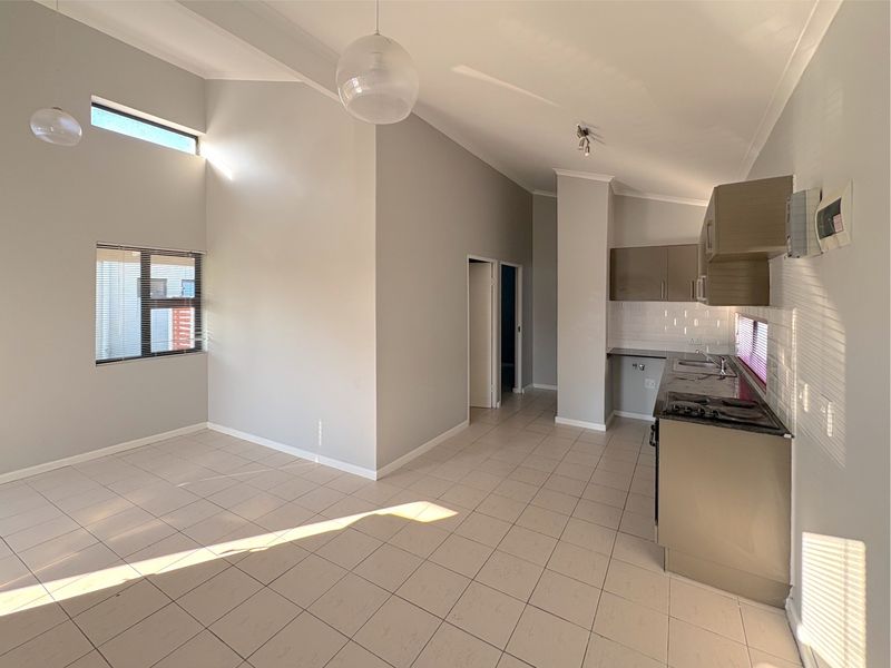 An open-plan living and kitchen area featuring tiled floors, vaulted ceilings, and a functional kitchen with built-in cabinetry and a gas hob.
