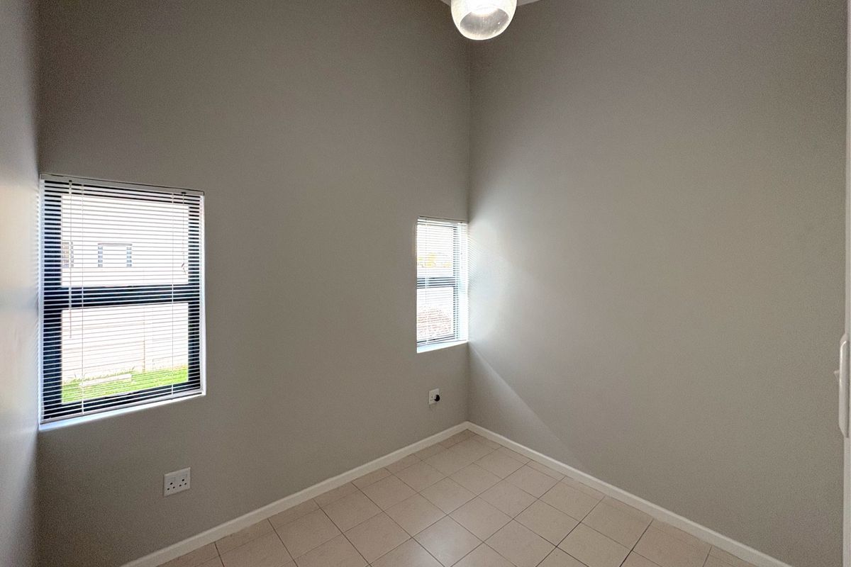 A clean, empty bedroom featuring neutral wall paint, tiled flooring, and two windows fitted with horizontal blinds.