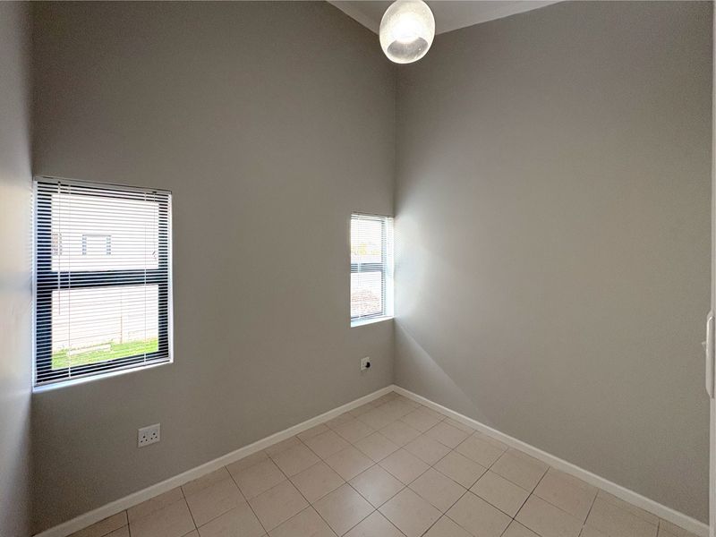 A clean, empty bedroom featuring neutral wall paint, tiled flooring, and two windows fitted with horizontal blinds.