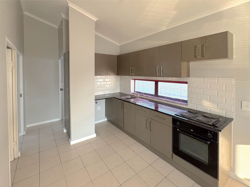 A clean, modern kitchen featuring neutral cabinetry, subway tile backsplash, integrated electric oven and hob, and durable ceramic floor tiles.