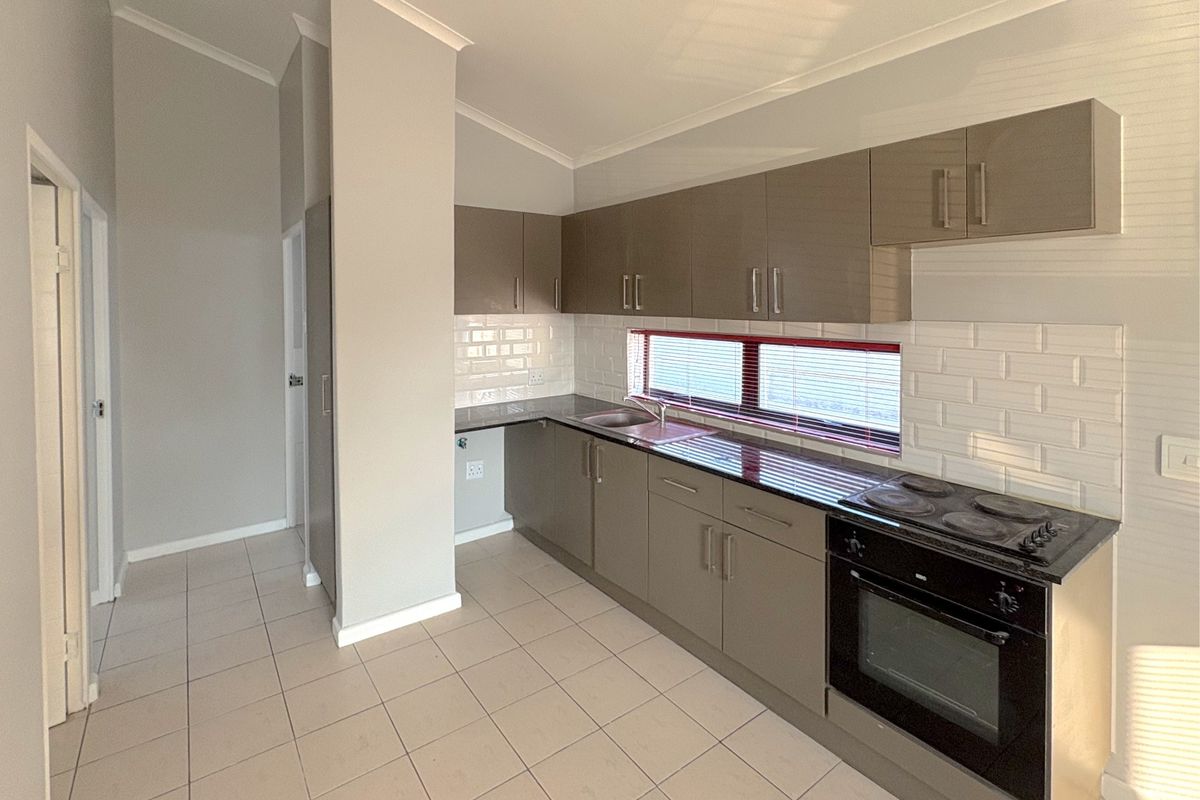 A clean, modern kitchen featuring neutral cabinetry, subway tile backsplash, integrated electric oven and hob, and durable ceramic floor tiles.