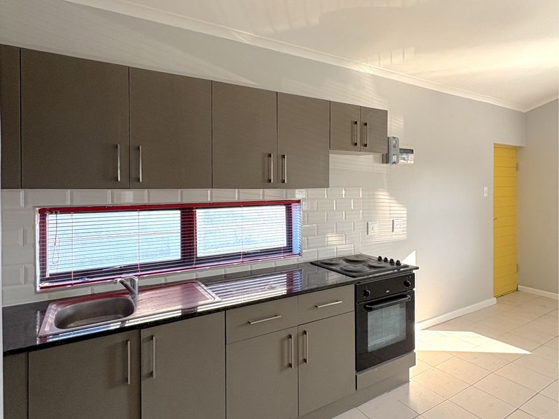 A clean, modern kitchen featuring grey cabinetry, a built-in oven and hob, subway tile backsplash, and neutral tiled flooring.