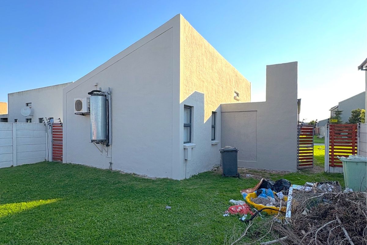 Rear view of the property featuring a lawn, solar geyser, air conditioning unit, and perimeter walling.