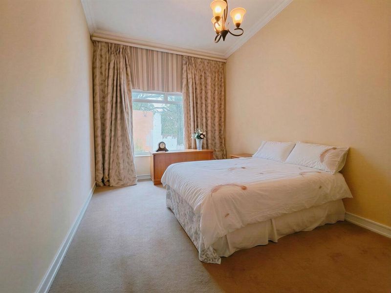 A well-proportioned bedroom featuring neutral wall tones, carpeted flooring, and a large window with floor-to-ceiling curtains.