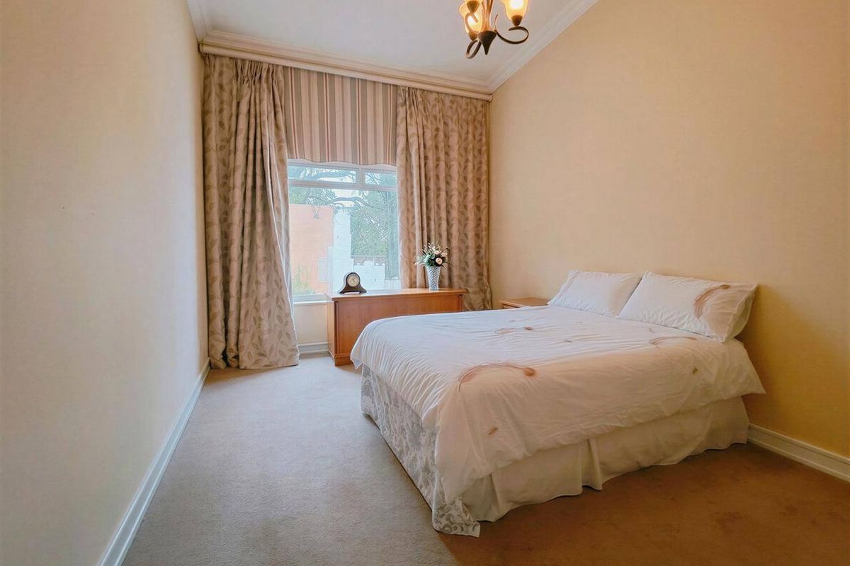 A well-proportioned bedroom featuring neutral wall tones, carpeted flooring, and a large window with floor-to-ceiling curtains.