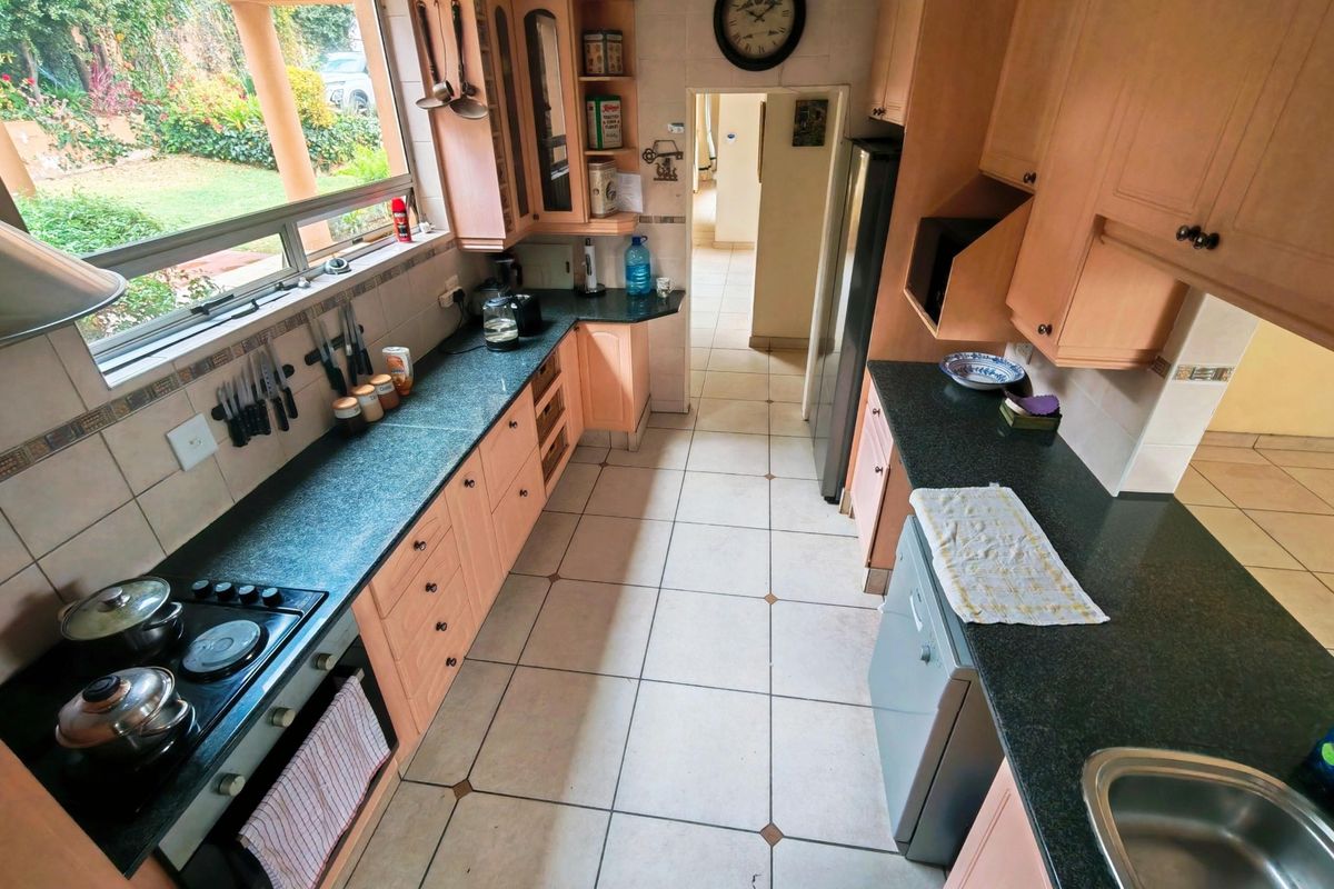 Functional kitchen featuring light wood cabinetry, dark granite countertops, built-in oven, hob, and tiled flooring with direct access to the garden area.