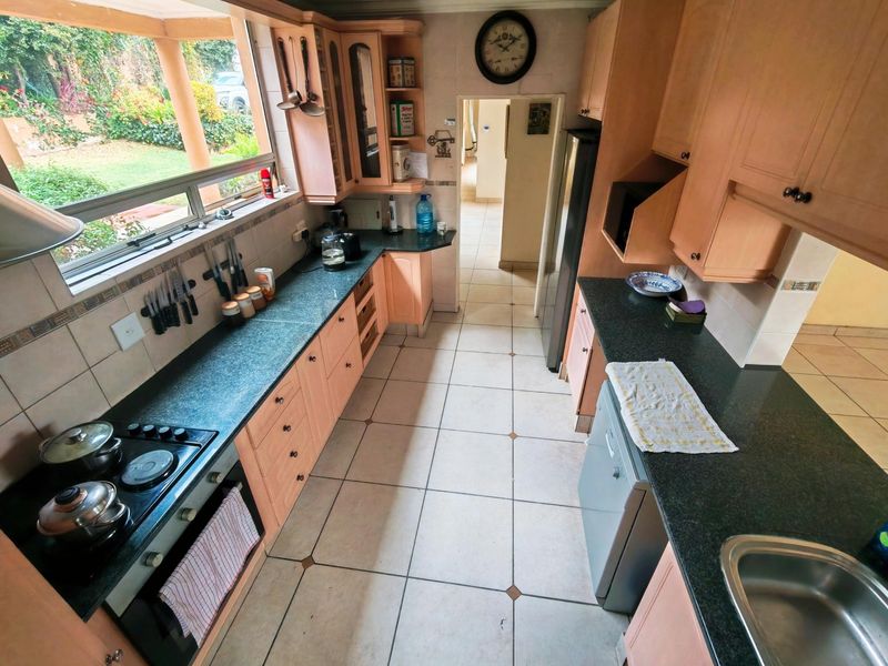 Functional kitchen featuring light wood cabinetry, dark granite countertops, built-in oven, hob, and tiled flooring with direct access to the garden area.