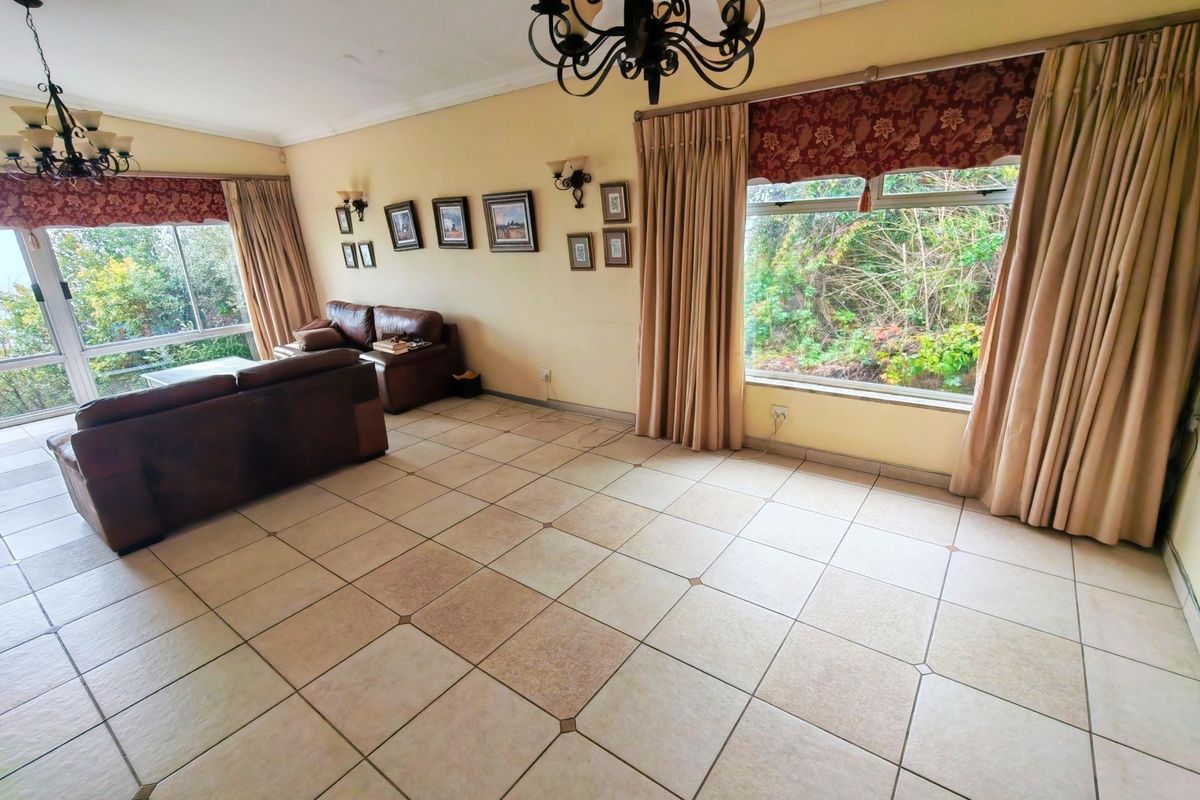 Spacious living room featuring large windows, tiled flooring, and classic chandelier lighting, offering a bright and functional space with garden views.