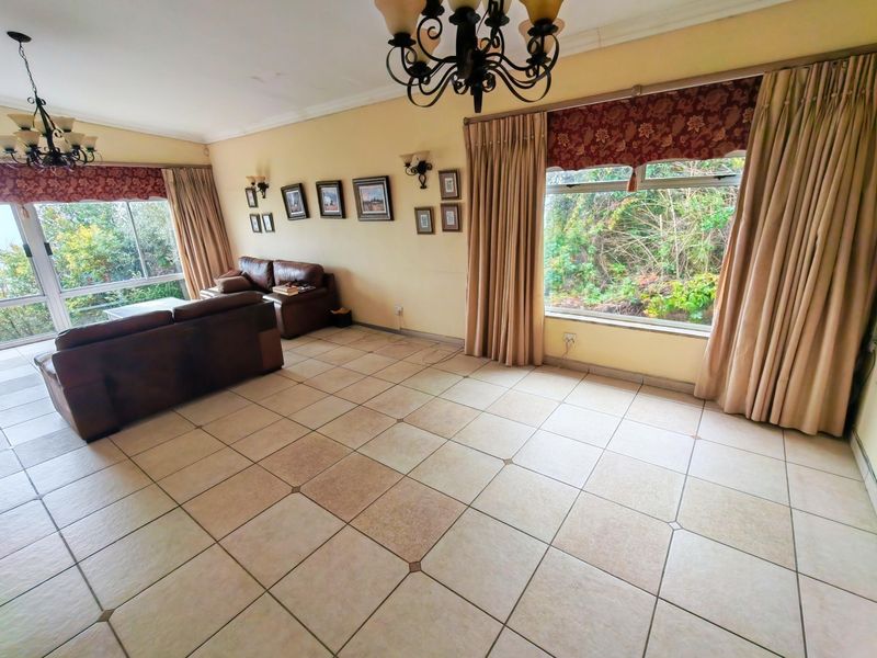 Spacious living room featuring large windows, tiled flooring, and classic chandelier lighting, offering a bright and functional space with garden views.