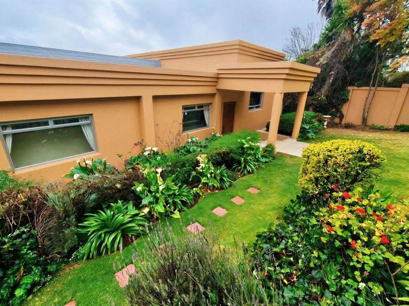 A well-maintained rear exterior view featuring a landscaped garden, paved walkway, and a covered patio area attached to the main house structure.