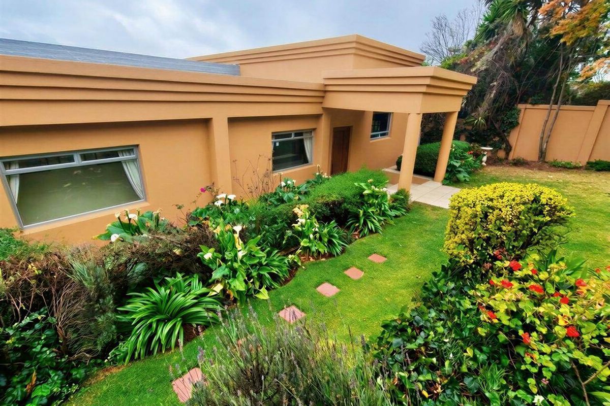 A well-maintained rear exterior view featuring a landscaped garden, paved walkway, and a covered patio area attached to the main house structure.