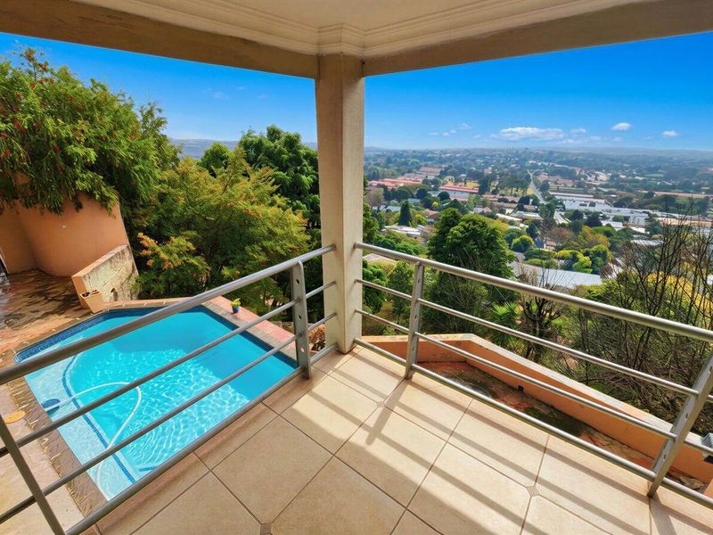 Covered balcony featuring tiled flooring and metal balustrades, overlooking a private swimming pool and expansive suburban landscape views.