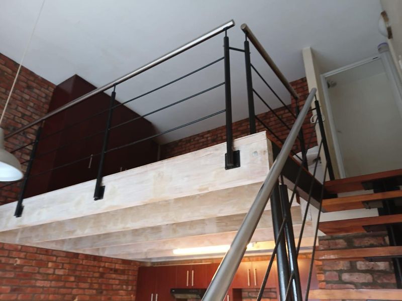 Open plan living area featuring a mezzanine level with metal balustrades, exposed brick walls, and a staircase with wooden treads.