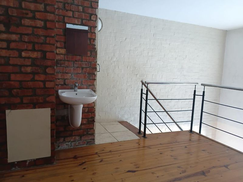 An open landing area featuring exposed brickwork, timber flooring, a pedestal basin, and a modern metal balustrade overlooking the lower level.