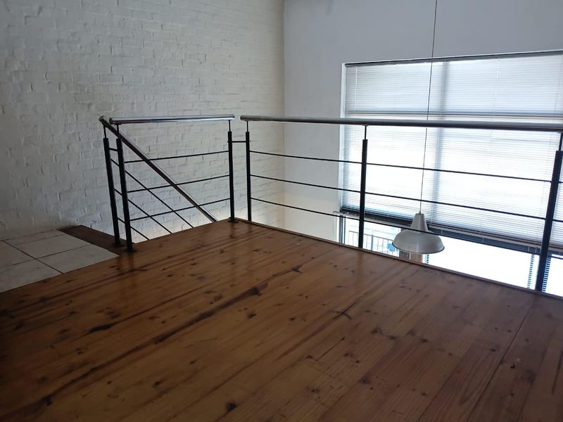 A mezzanine level bedroom area featuring polished timber flooring, an exposed white brick wall, and a modern metal balustrade overlooking the lower level.