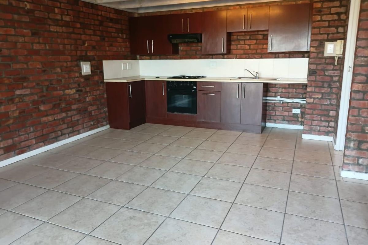 Open plan kitchen featuring exposed brick walls, tiled flooring, and dark wood cabinetry with built-in oven and hob.