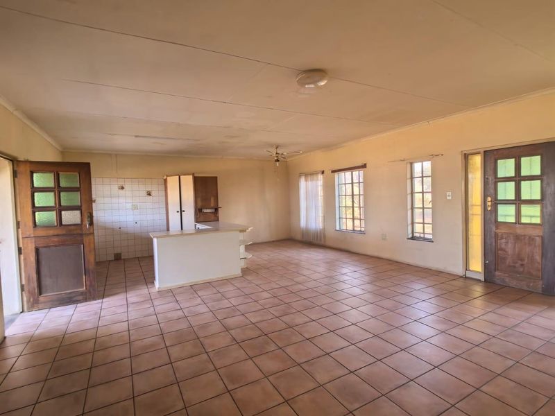 Spacious open-plan living and kitchen area featuring tiled flooring, a central island, and direct access through timber-framed doors.