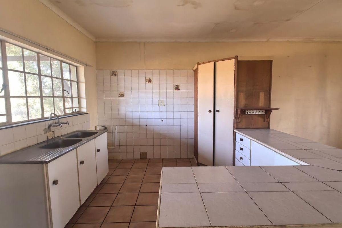 An empty, dated kitchen featuring tiled countertops, double bowl sink, and built-in cabinetry, requiring renovation to update finishes and address ceiling water damage.