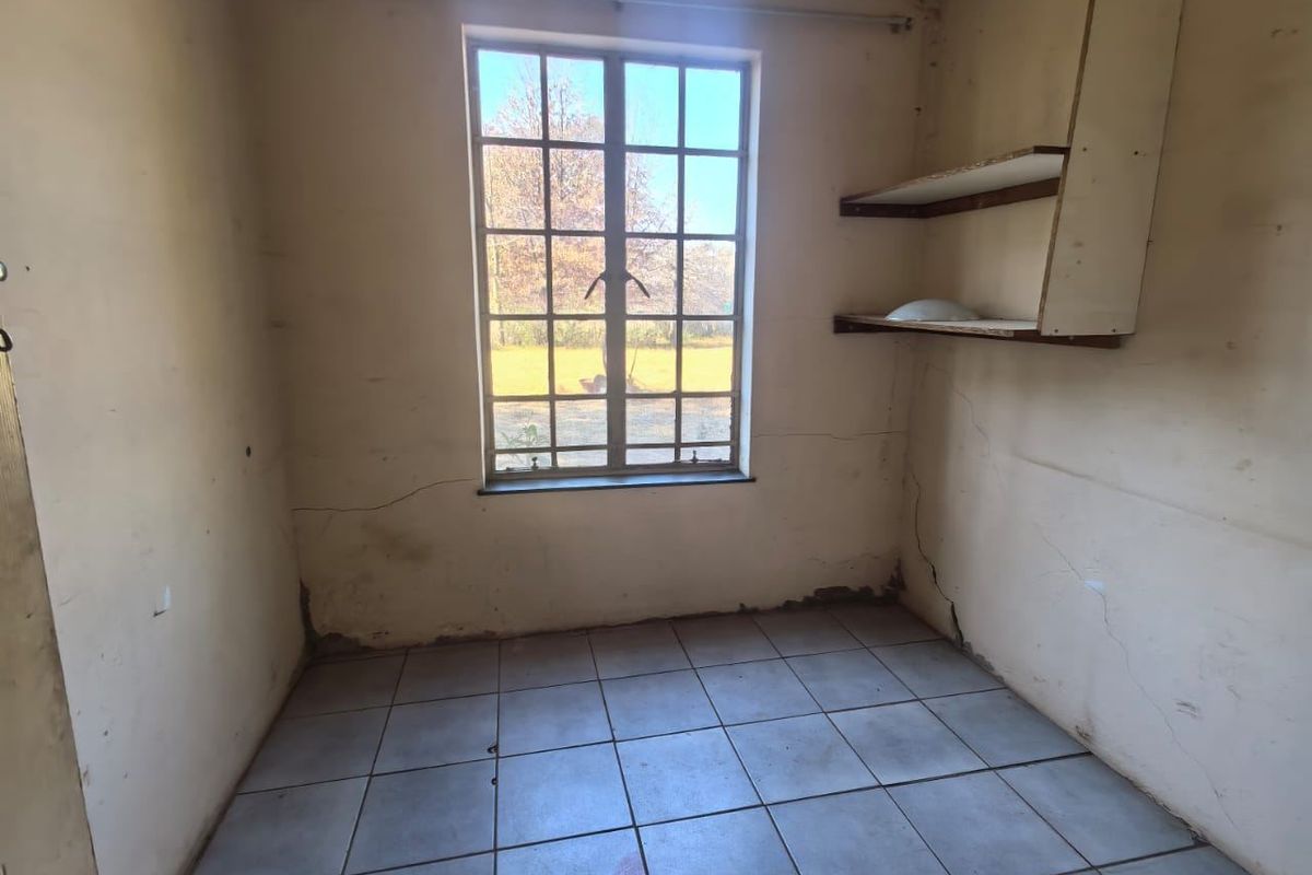 An empty bedroom featuring tiled flooring, a grid-pane window, and built-in wall shelving, requiring cosmetic updates to the walls.