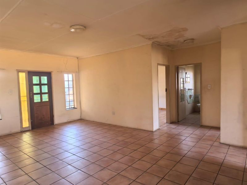 An empty living room featuring tiled flooring, a timber front door, and visible ceiling water damage requiring repair.
