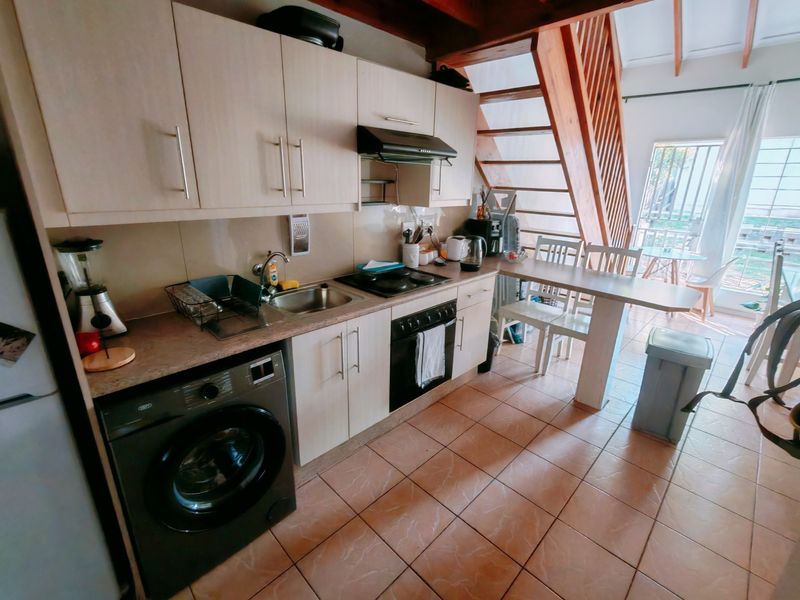 Compact kitchen featuring light-toned cabinetry, integrated appliances, tiled flooring, and an adjacent timber staircase leading to the upper level.