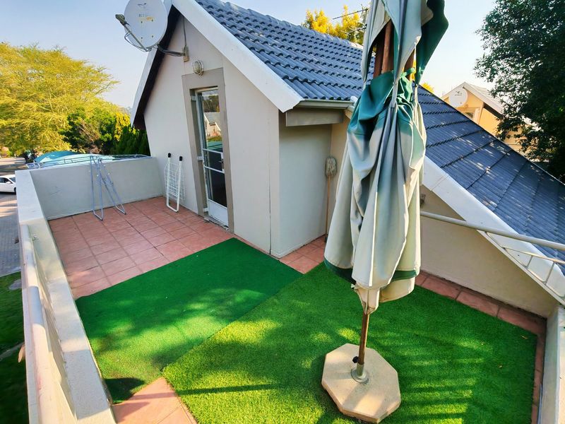 An elevated balcony area featuring a mix of tiled flooring and artificial turf, providing an open outdoor space accessible from the upper level.